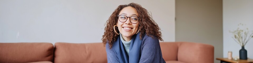 Obraz premium Young african female smiling on sofa with glasses in cozy living room setting