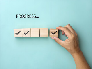 Hand places wooden cube with check mark, shows progress steps, and signifies moving forward on a task or goals on light blue background.