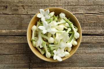 Beautiful jasmine flowers in bowl on wooden table, top view