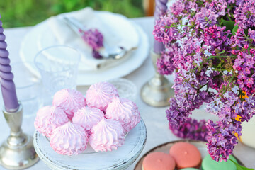 Beautiful lilac flowers, sweets, plates, cutlery and candles on table in garden, closeup