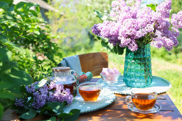 Beautiful lilac flowers, sweets and tea on wooden table in garden