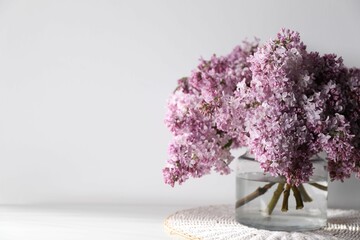 Beautiful lilac flowers in glass vase on table near white wall indoors, closeup. Space for text