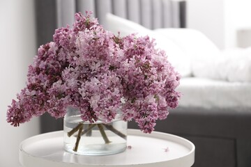 Beautiful lilac flowers in glass vase on table indoors, space for text