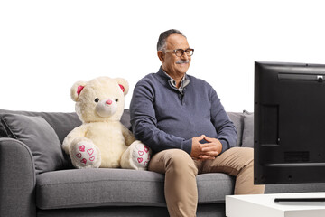 Mature man with a teddy bear sitting on a sofa and watching tv