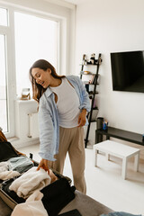 Woman standing and smiling while packing things into a suitcase in the living room