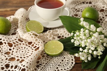 Beautiful lilies of the valley flowers, tea and limes on wooden table, closeup