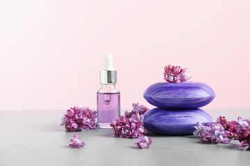 Soap bars, essential oil and lilac flowers on grey table against pink background, closeup