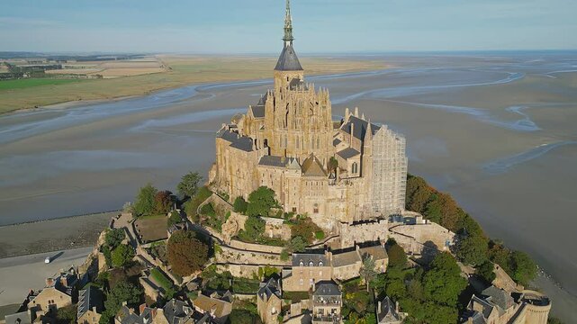 Mont-Saint-Michel Abbey with tidal landscape and rural fields in the background, on a sunny day