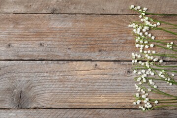 Fototapeta premium Beautiful lily-of-the-valley flowers on wooden background, flat lay. Space for text