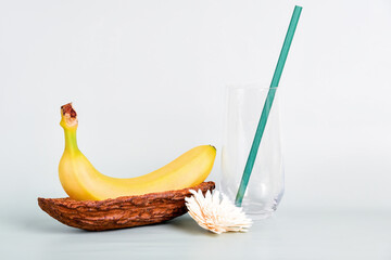 Banana in a cocoa pod alongside a glass with a green straw and decorative flower. Tropical and exotic vibe