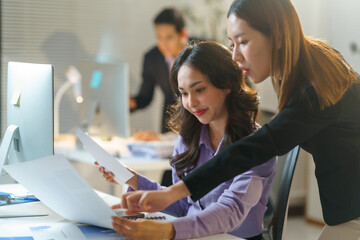 Two businesswomen analyzing financial charts and documents in a modern office, collaborating on a project and pointing at paperwork