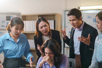 Asian businesspeople arguing with a stressed colleague in an office meeting room, showcasing tension and conflict among the team