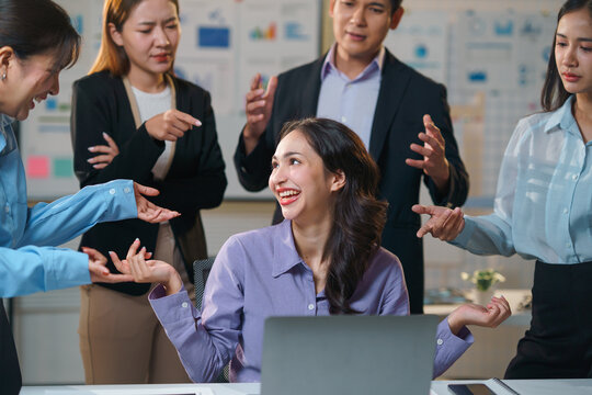 Asian business team blaming and criticizing young businesswoman at her desk with laptop in office meeting
