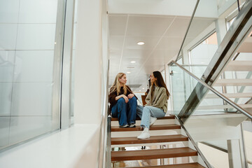 Two female friends sitting on the stairs and looking at each other, indoors
