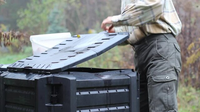Compost. Man throws kitchen scraps into a composter.