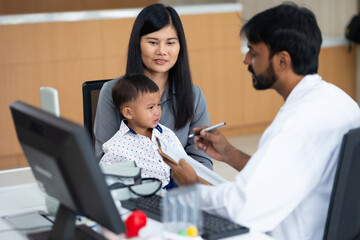 pediatrician : Indian male Doctor working with little asian boy patient and family at hospital and wellness center.