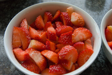 A vibrant bowl brimming with freshly sliced strawberries, their rich red hues and juicy texture...