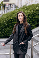 Fototapeta premium Charming brunette with long brown hair poses for the camera in a leather jacket and jeans outdoors in Spring