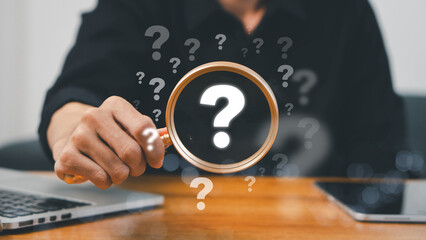 A hand holding a magnifying glass over large question marks surrounded by smaller ones symbolizes cause analysis and problem-solving. Question mark and root cause analysis concept. solution, analyze