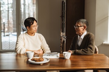 A grandfather sits at a table and talks to his son who sits next to him