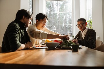Grandfather, son, and grandson sitting at the table cooking while smiling