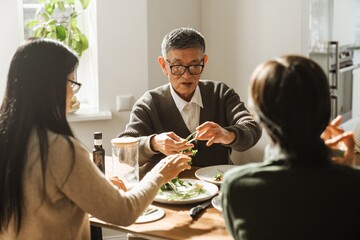 Grandfather and grandmother sitting at a table holding greens while their grandson sits next to them