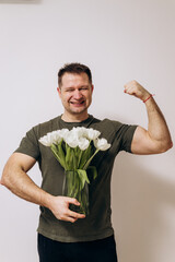 A manly guy in a green t-shirt holds a bouquet of white tulips and congratulates the girls