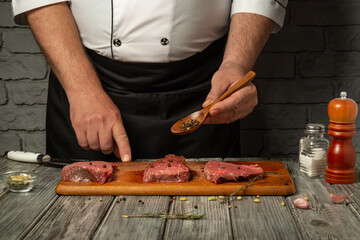 A skilled chef is seasoning three cuts of raw beef on a wooden board with a wooden spoon. The kitchen has a cozy ambiance with stone walls and cooking utensils visible
