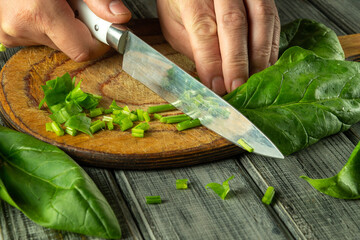 Hands skillfully chop fresh spinach on a wooden cutting board, preparing a vitamin-rich meal in a...