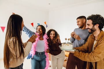 A group of five friends laughing while one of them holds a cake