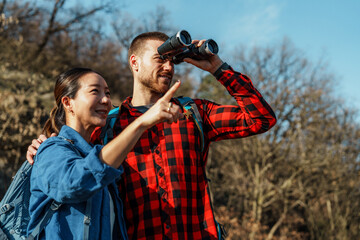 Hikers are exploring the wilderness, observing nature with binoculars while the woman points her finger towards something interesting in the distance