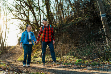 Fototapeta premium Hikers holding hands while walking along a scenic path in the woods, soaking in the fresh air and basking in sunlight filtering through the lush trees, celebrating their connection