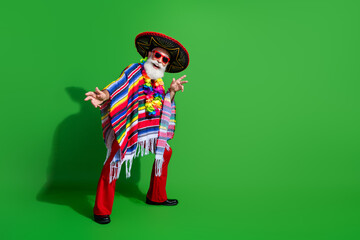 Festive senior man in colorful traditional Mexican attire dancing on a vibrant green background