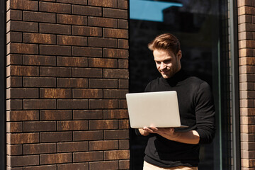 Handsome man enjoying a stroll while working on his laptop in a vibrant urban setting