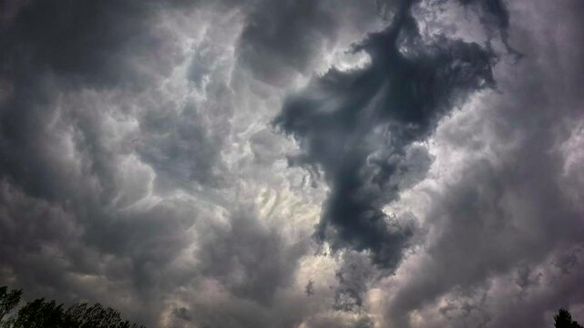 Dark foreboding storm clouds roll quickly across the sky bringing rain to the spring trees and foliage. Time Lapse.