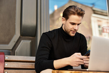 Handsome man enjoys a leisurely walk while using his phone outside a coffee shop