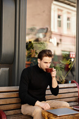 Handsome man enjoying a warm drink while seated on a bench in a lively urban setting