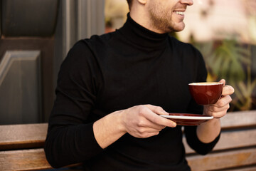 Handsome man enjoying a warm drink while strolling through a charming outdoor cafe