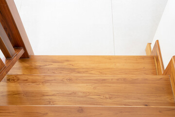Close up image of teak wood stairs with beige tiled floor and white wall