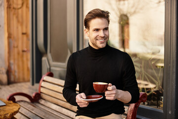 Handsome man sipping coffee while enjoying a leisurely walk in a charming cafe setting