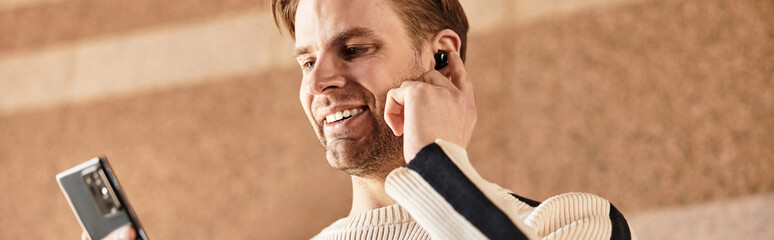 Obraz premium Handsome man enjoying a leisurely walk while using his smartphone and earbuds outdoors