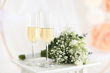 Glasses of champagne and wedding bouquet on table indoors, closeup