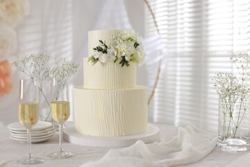 Delicious wedding cake with floral decor and glasses of champagne on table indoors