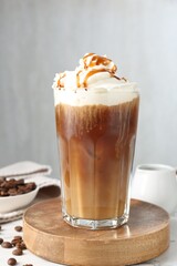 Tasty iced coffee with whipped cream, syrup and beans on white table
