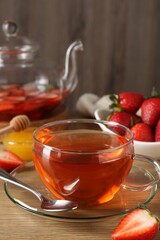 Aromatic fruit tea with strawberries and honey on wooden table, closeup
