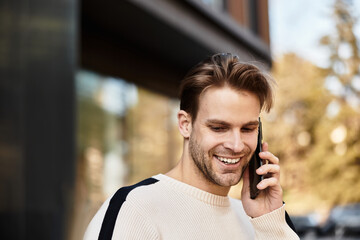 Handsome man smiles warmly while walking and talking on his phone in a vibrant urban setting