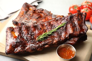 Tasty roasted pork ribs served with rosemary, tomatoes and sauce on light grey table, closeup