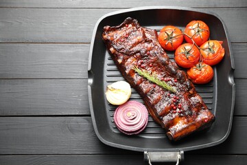 Delicious roasted pork ribs with rosemary, tomatoes and onions on grey wooden table, top view. Space for text