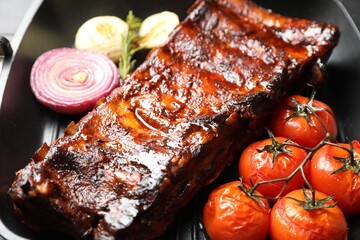 Delicious roasted pork ribs with tomatoes and onions on grill pan, closeup