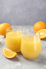 Orange juice in glasses and fresh fruits on grey table, closeup